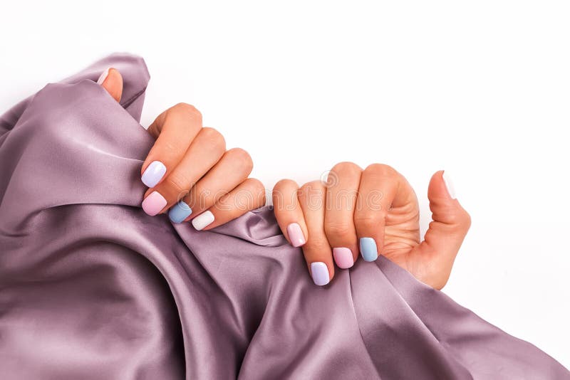 Woman`s hands close-up with beautiful professional manicure of different pastel colors holding a silk cloth stock photography