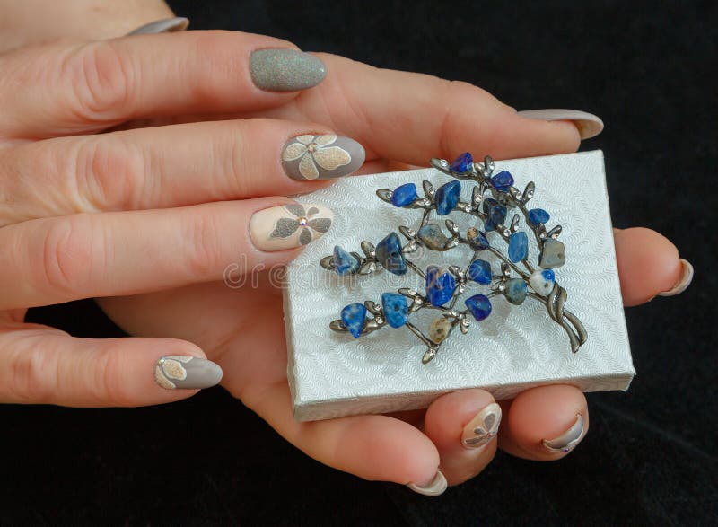 Female hands with a multicolored manicure and a brooch with blue stones closeup royalty free stock image