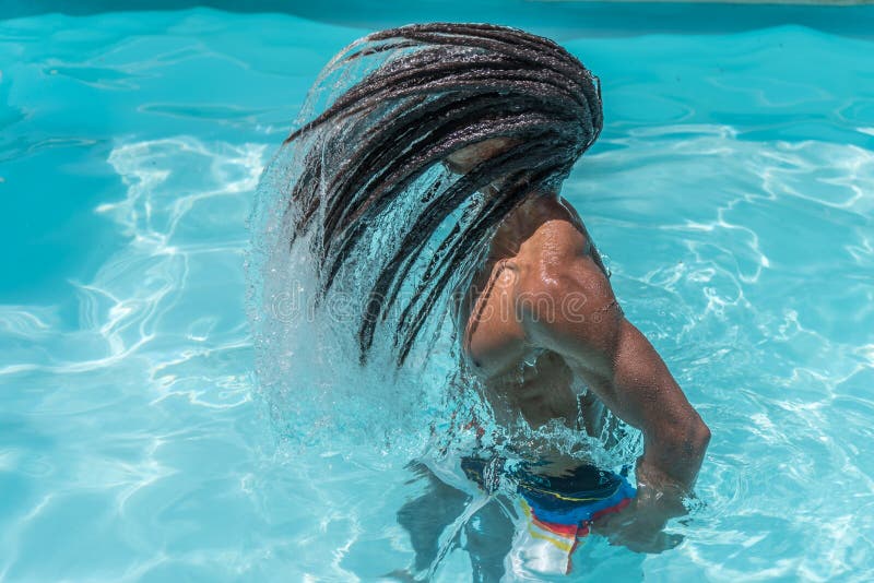Young black man with dreadlocks inside a pool moving his wet hair in a trail of water. High quality photo royalty free stock photography