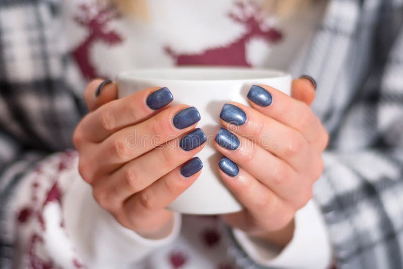 Female hands with navy blue manicure color holding cup of tea stock images